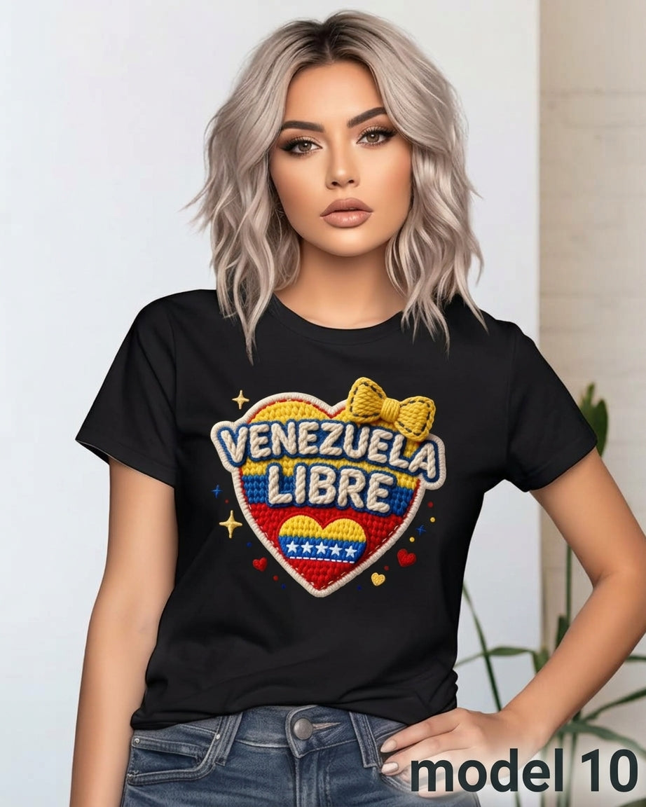 A woman wearing a black graphic t-shirt with a 'Venezuela Libre' heart design in red, white, and blue, paired with blue jeans. The background is a clean, light-colored indoor setting.