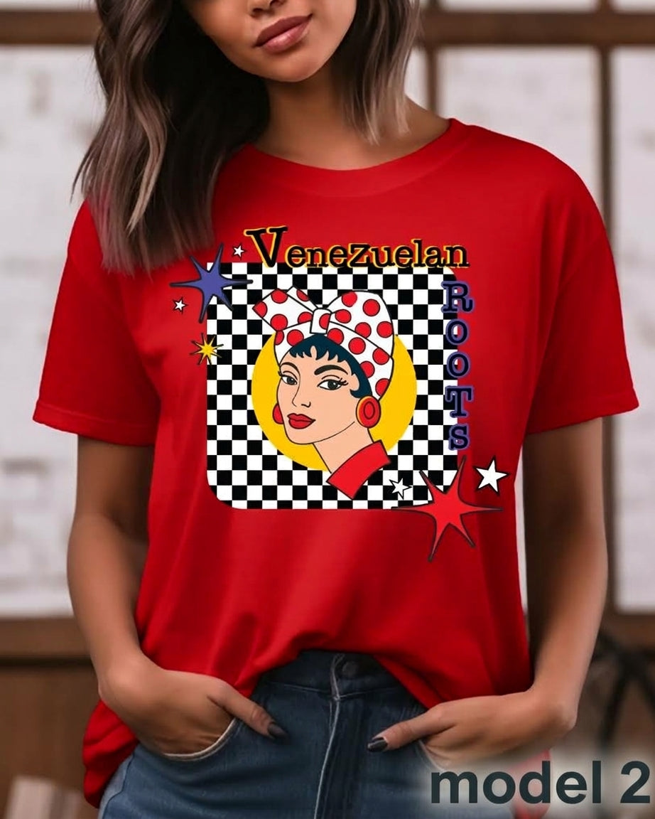 A woman wearing a red graphic t-shirt with a Venezuelan-themed pop-art design featuring a woman in a red polka-dot headband, a yellow crescent moon, and the text 'Venezuelan Roots'.